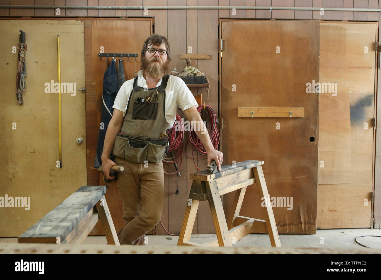 Ritratto di fiducioso falegname con gli strumenti di lavoro in piedi in officina Foto Stock