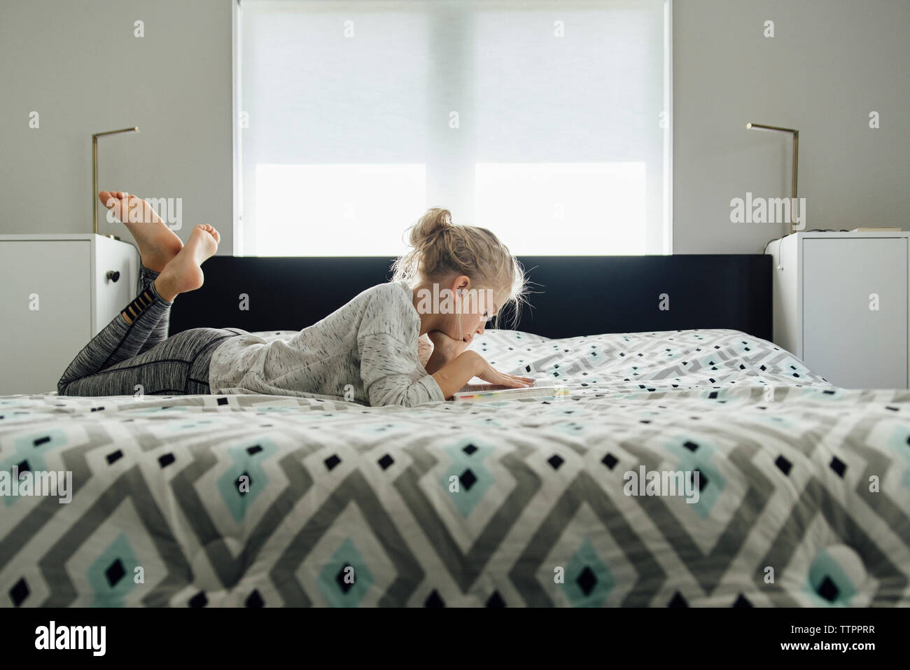Vista laterale della lettura della ragazza prenota mentre giaceva sul letto di casa Foto Stock