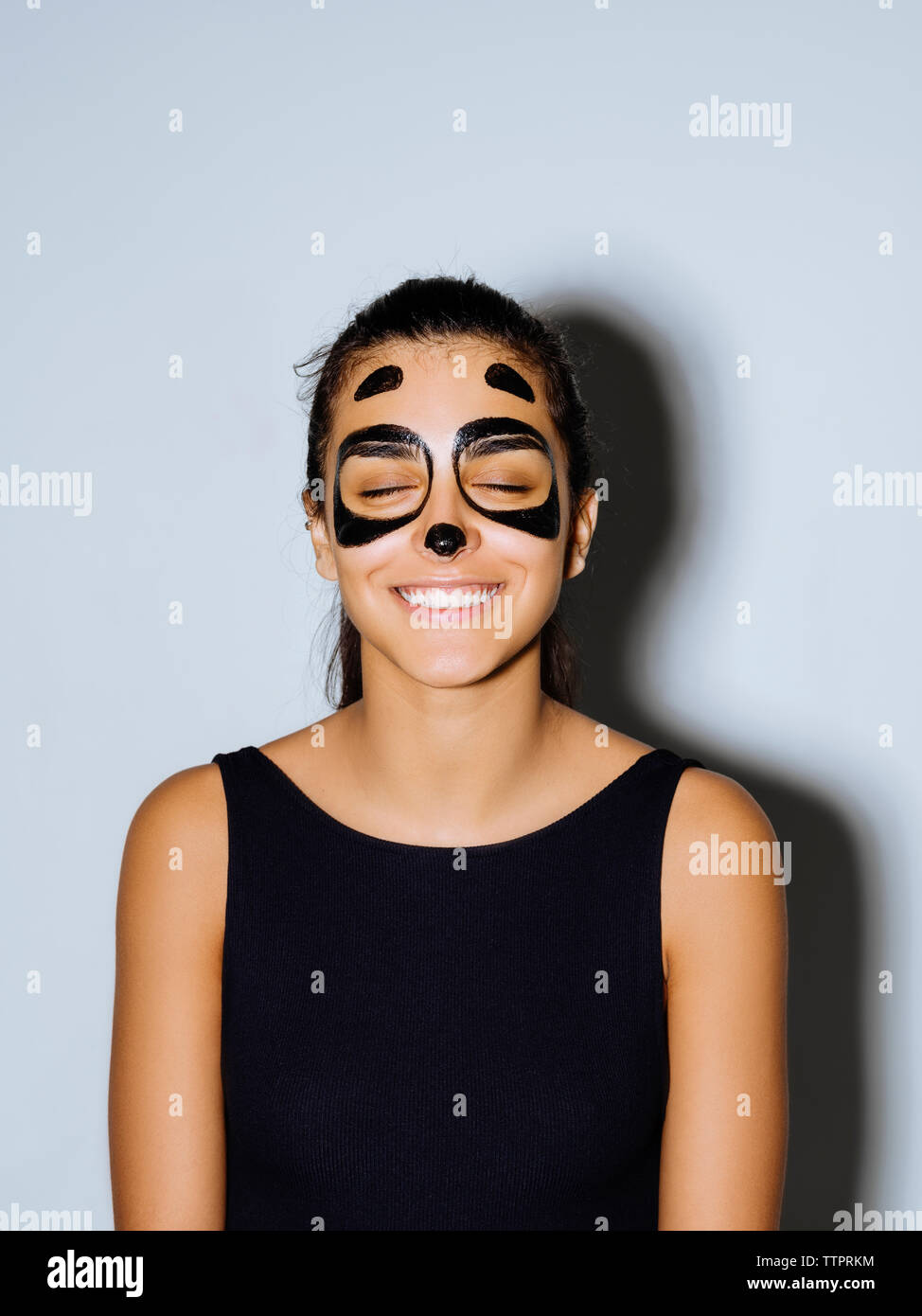 Close-up di donna felice con gli occhi chiusi e faccia permanente di vernice contro la parete Foto Stock
