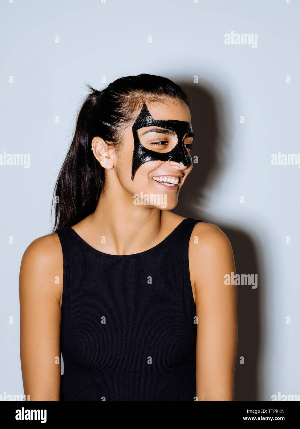 Close-up di donna felice con vernice faccia guardando lontano in piedi contro la parete Foto Stock