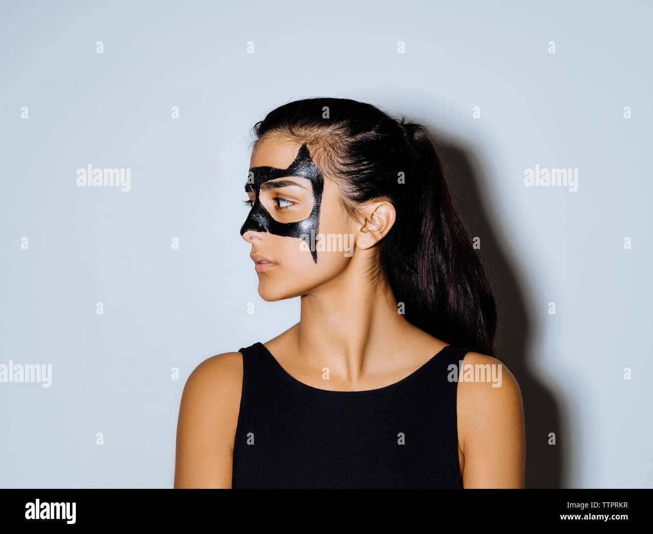 Close-up di donna con vernice faccia guardando lontano in piedi contro la parete Foto Stock