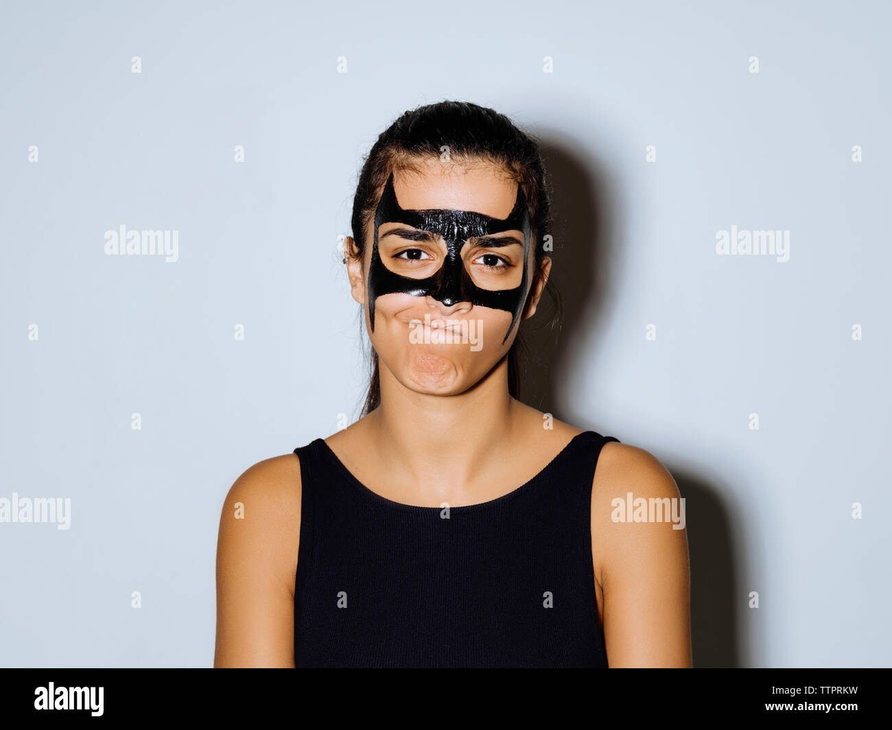 Close-up ritratto di donna con vernice nera rendendo faccia mentre in piedi contro la parete Foto Stock