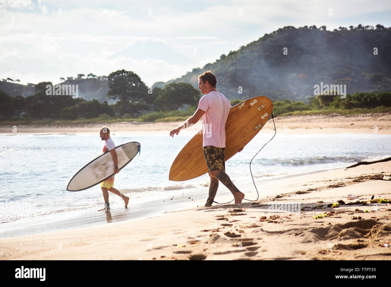 Vista laterale dei maschi di surfers che trasportano le tavole da surf mentre passeggiate sulla spiaggia Foto Stock