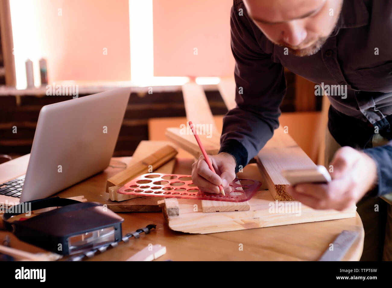 Falegname con telefono mobile lavora in officina Foto Stock
