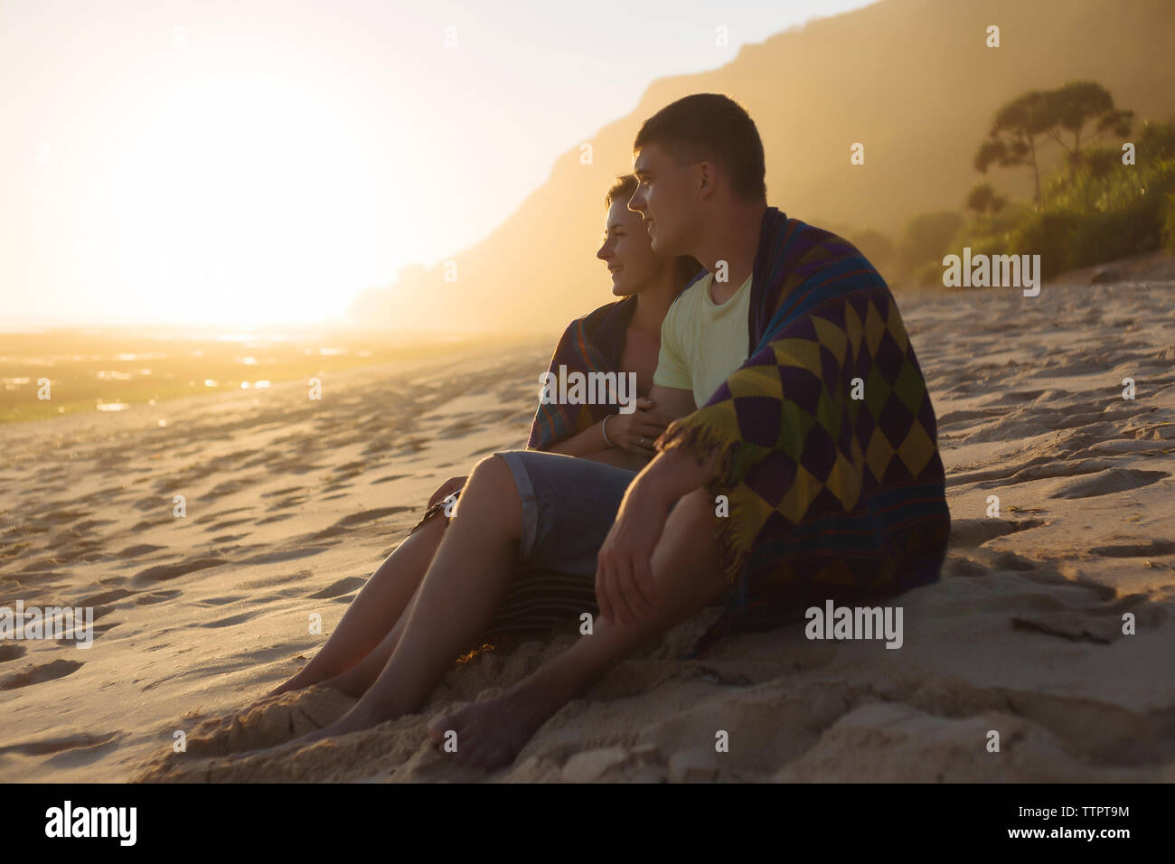 Coppia giovane avvolto in una coperta mentre cerchi di distanza alla spiaggia durante il tramonto Foto Stock