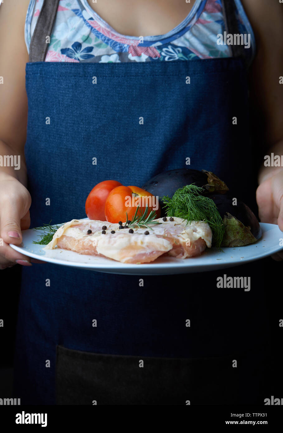 Sezione mediana della donna che mantiene la carne di pollo con verdure nella piastra Foto Stock