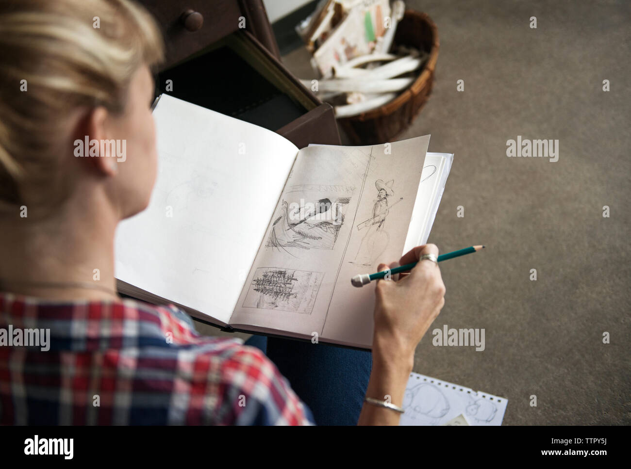 Artista femminile guardando i bozzetti in libro seduti a casa Foto Stock