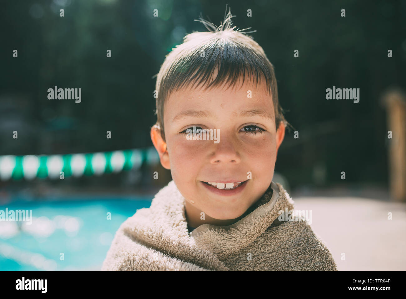 Ritratto di felice ragazzo avvolto in un asciugamano in piedi sul bordo della piscina Foto Stock