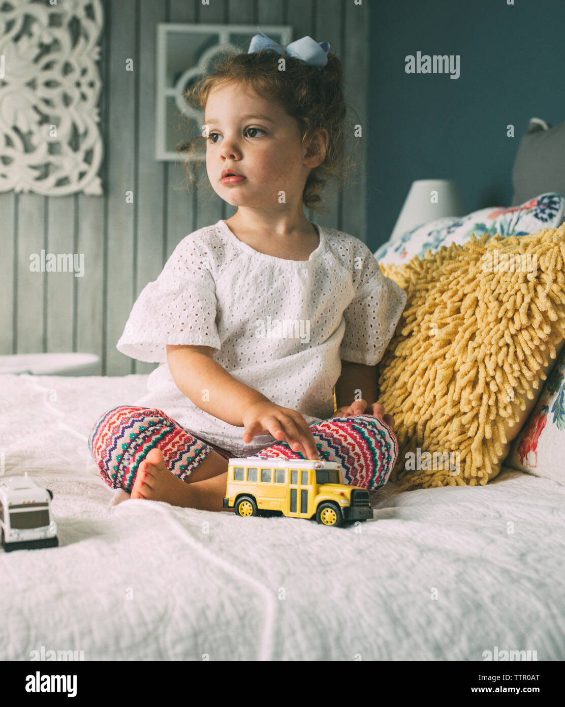 Premurosa ragazza con giocattoli seduta sul letto Foto Stock