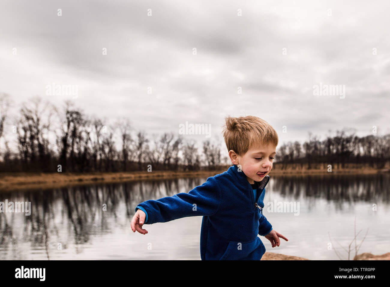 Ragazzo giovane essendo stupido sul bordo di un lago in un giorno nuvoloso Foto Stock