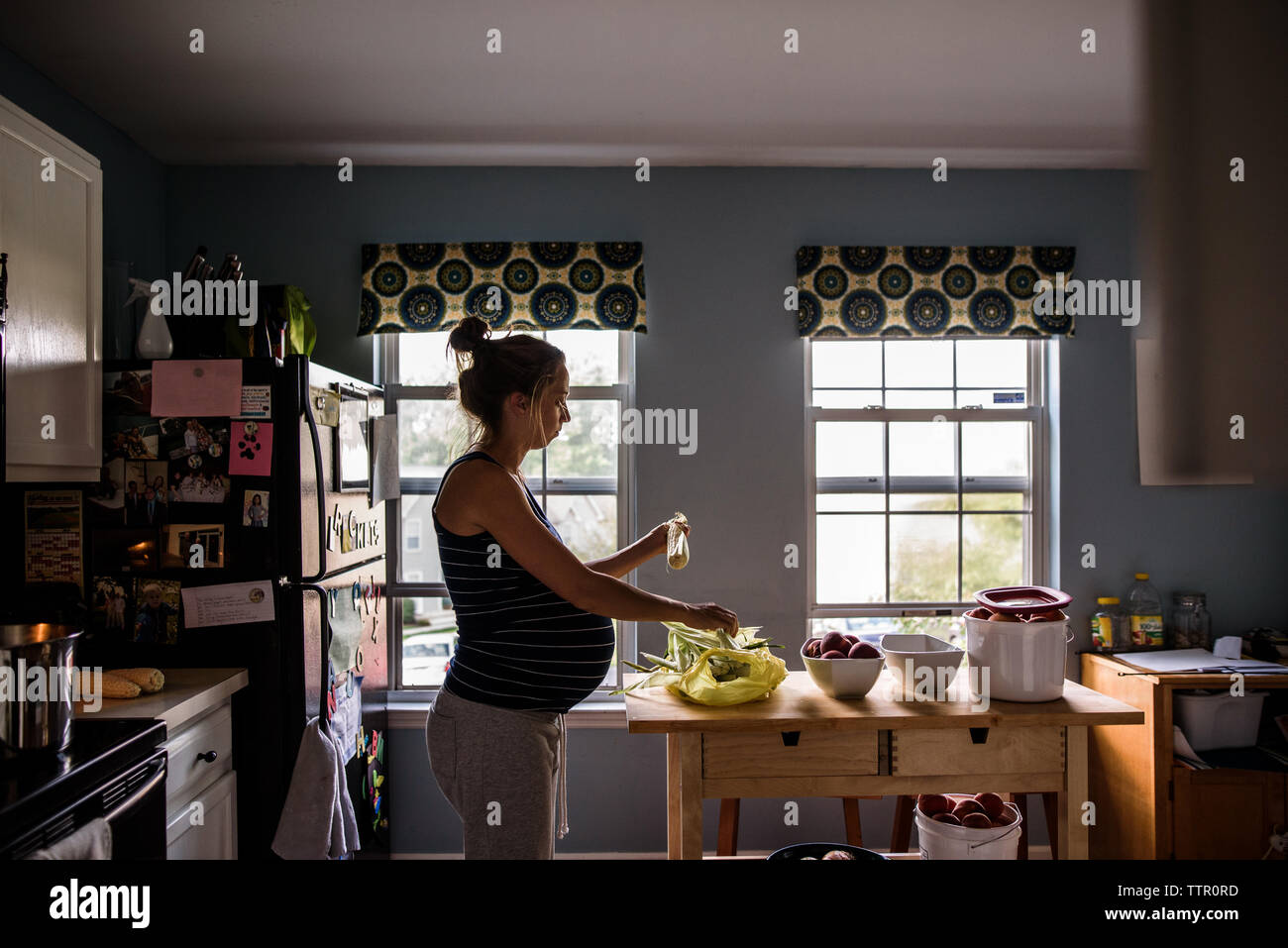 Madre in attesa shucking mais in luminosa cucina Foto Stock