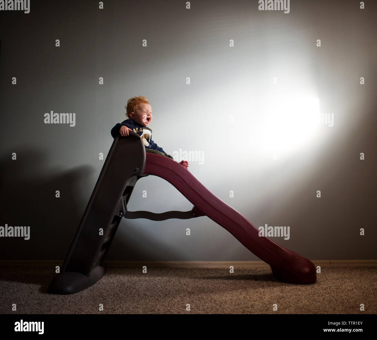 Allegro baby boy scorrevole sulla slitta contro la parete a casa Foto Stock