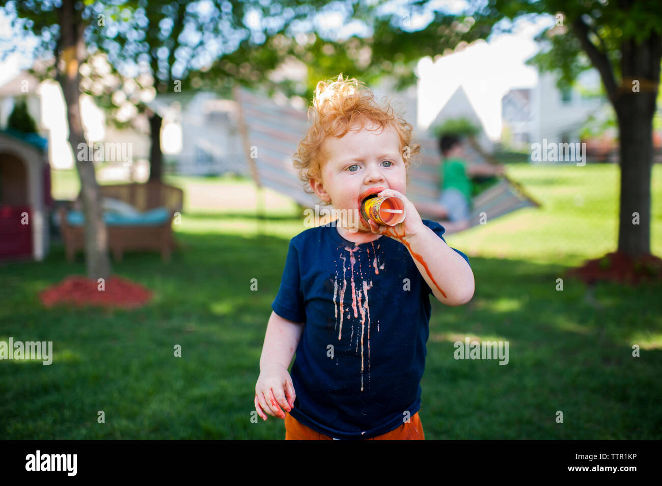 Carino baby boy a mangiare il gelato mentre si sta in piedi sul campo erboso in cantiere Foto Stock
