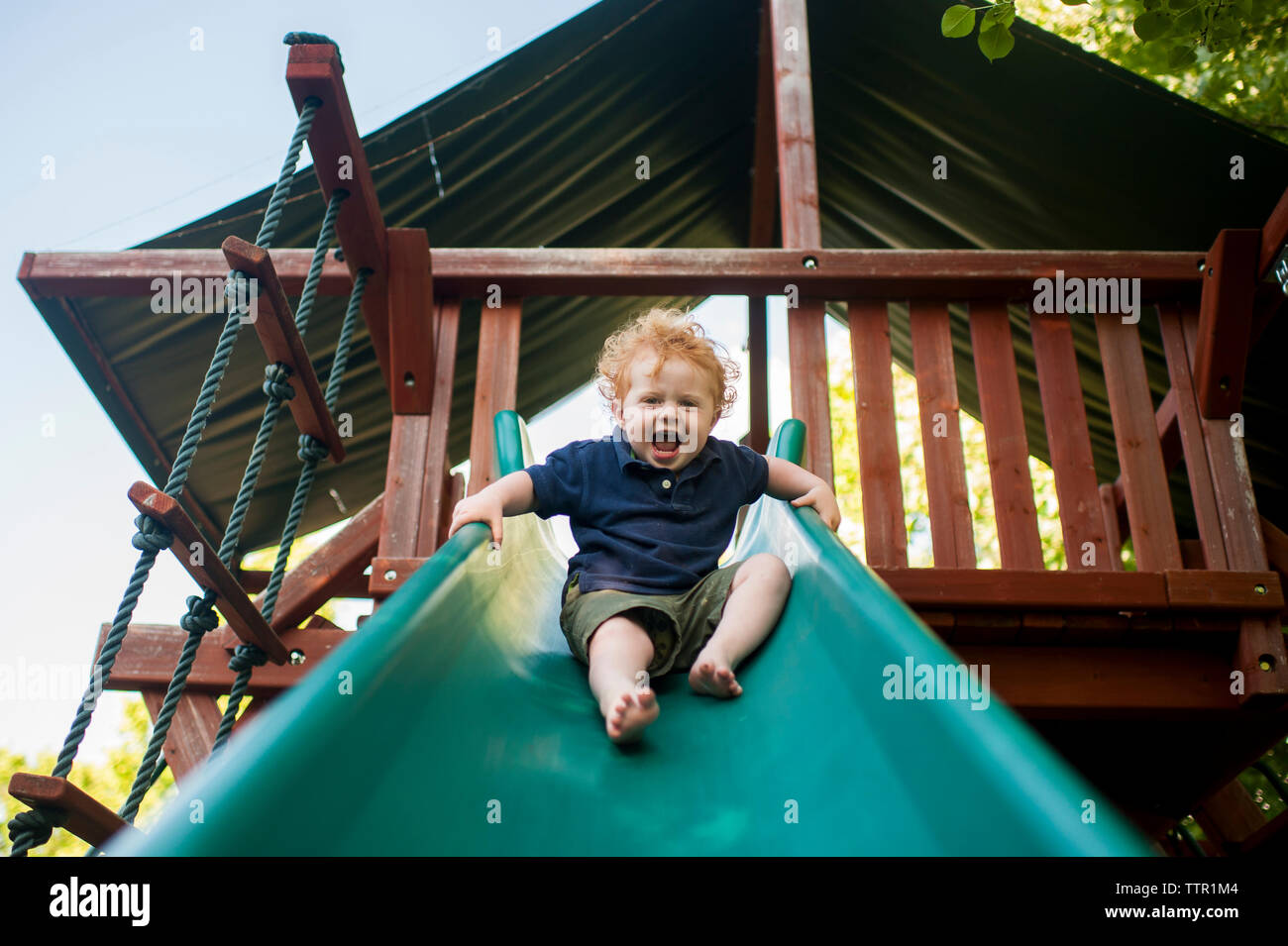 Angolo basso ritratto di happy baby boy urlando mentre lo scorrimento in cantiere Foto Stock