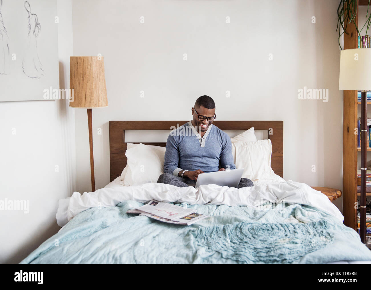 Uomo con notebook mentre si siede sul letto di casa Foto Stock