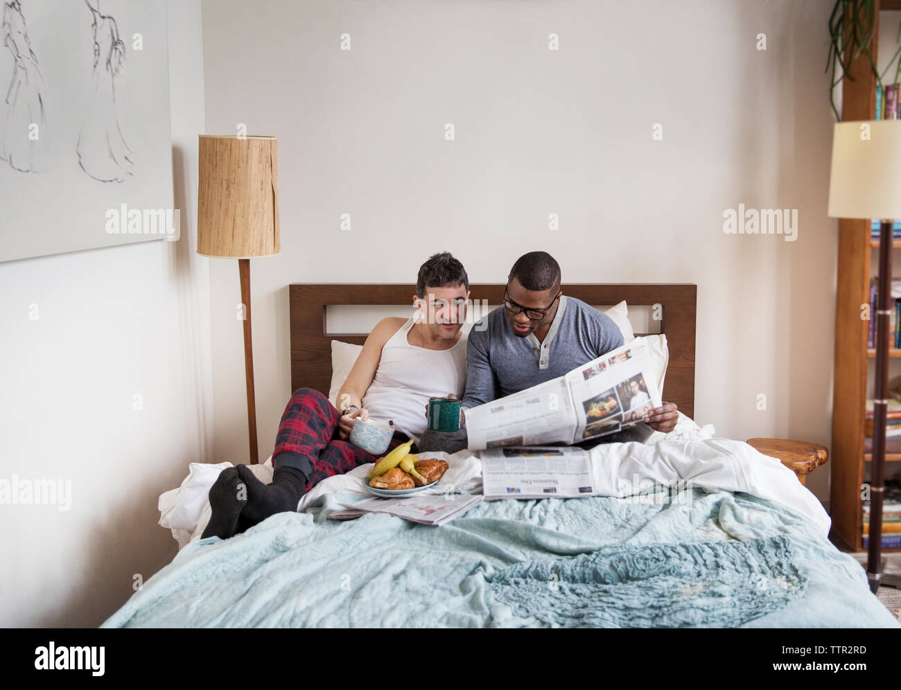 Multi-etnico maschi omosessuali leggendo il giornale in camera da letto Foto Stock