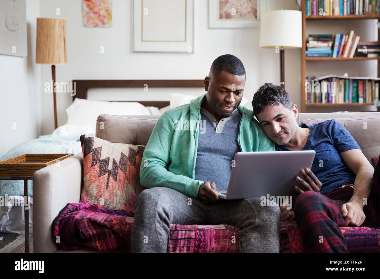 Multi-etnico maschi omosessuali utilizzando computer portatile sul divano di casa Foto Stock