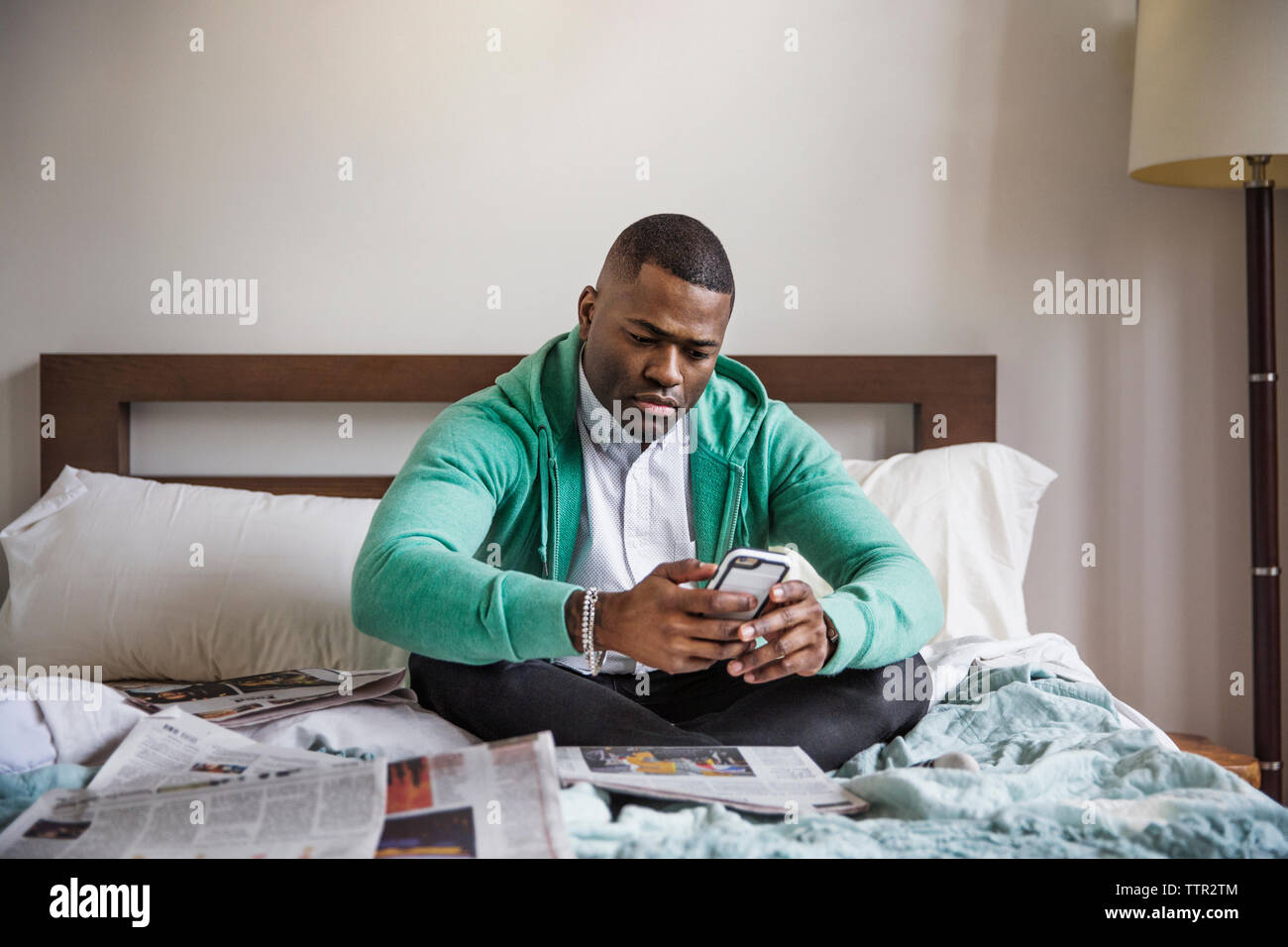 Uomo che utilizza smart phone mentre è seduto sul letto di casa Foto Stock