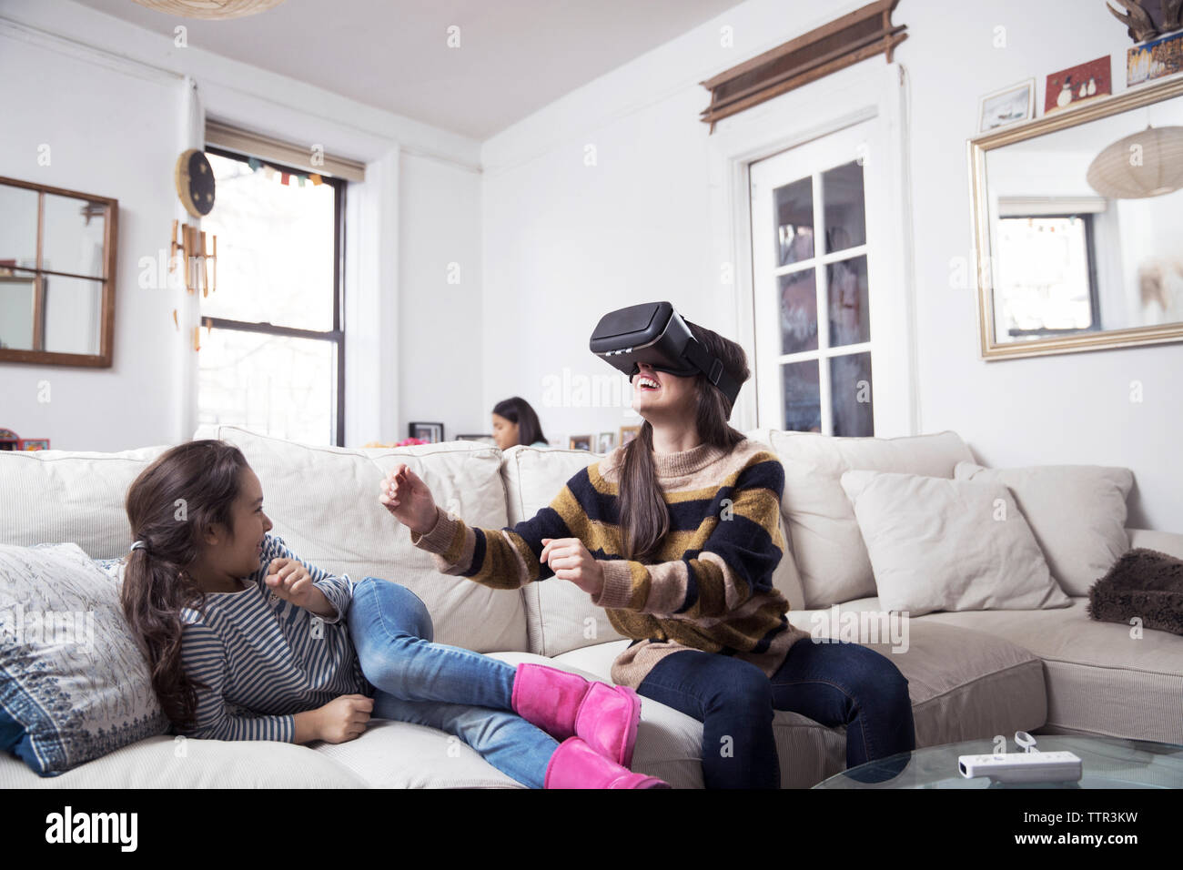 Figlia guardando madre godendo la realtà virtuale simulatore mentre seduto sul divano Foto Stock