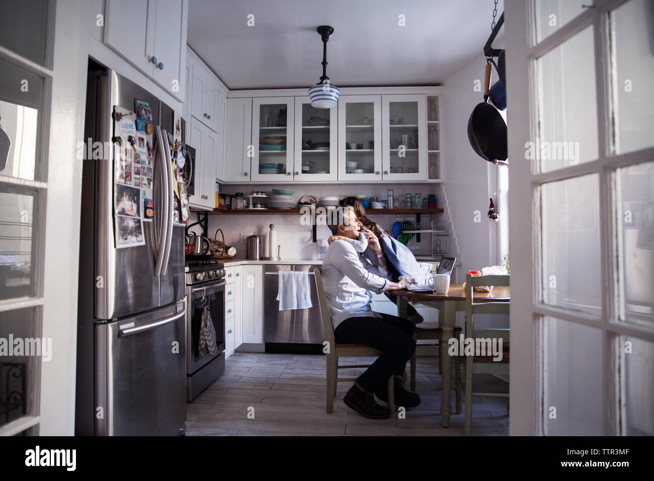 La Figlia che abbraccia il padre utilizzando il computer portatile in cucina a casa Foto Stock