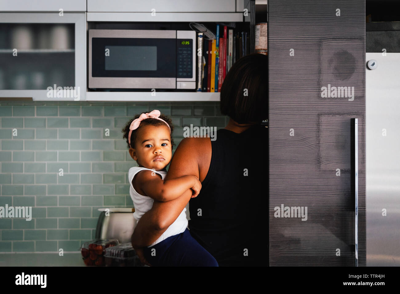 Vista posteriore della madre che trasportano carino figlia mentre in piedi in cucina a casa Foto Stock