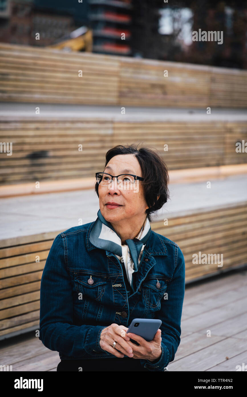 Premurosa donna senior con smart phone che guarda lontano seduti sui sedili in città Foto Stock