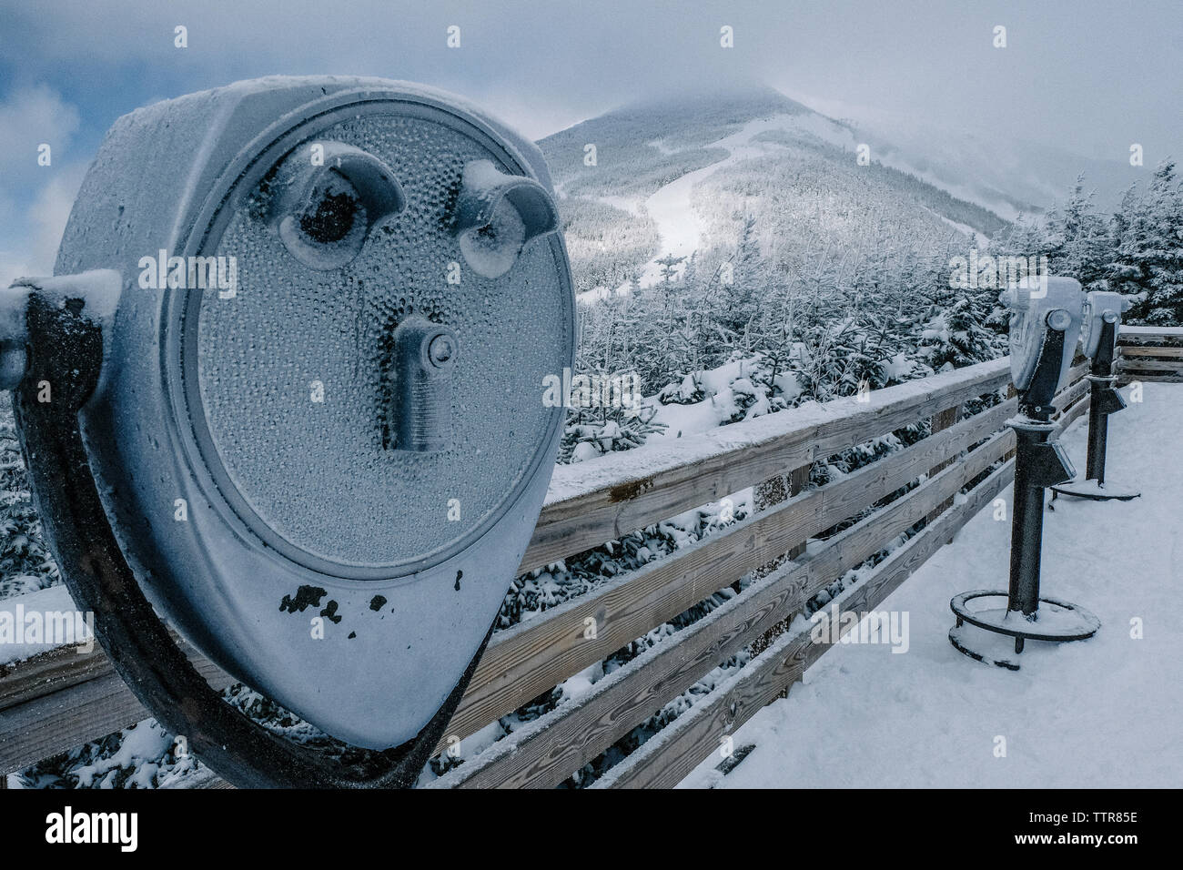 Coperta di neve gettoniera binocolo contro le montagne in punto di osservazione Foto Stock