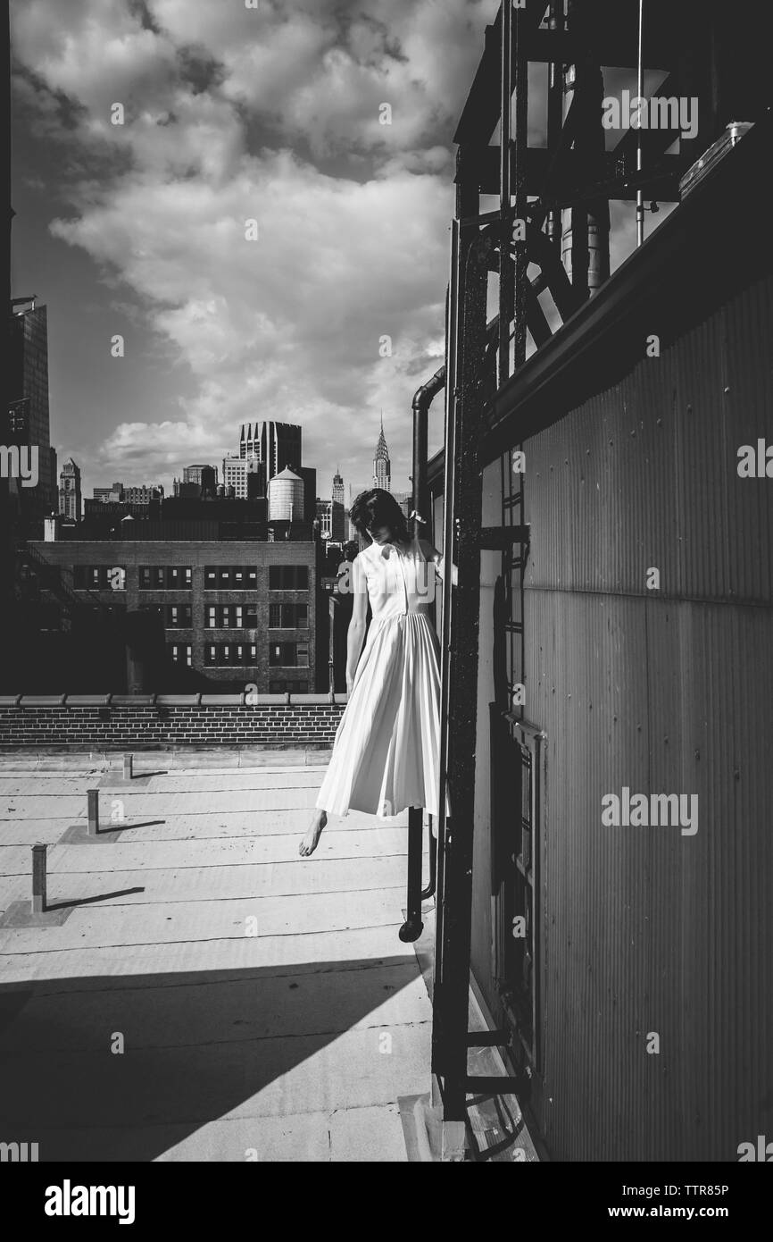 Donna in piedi sulla scala dell'edificio terrazza contro il cielo in città Foto Stock