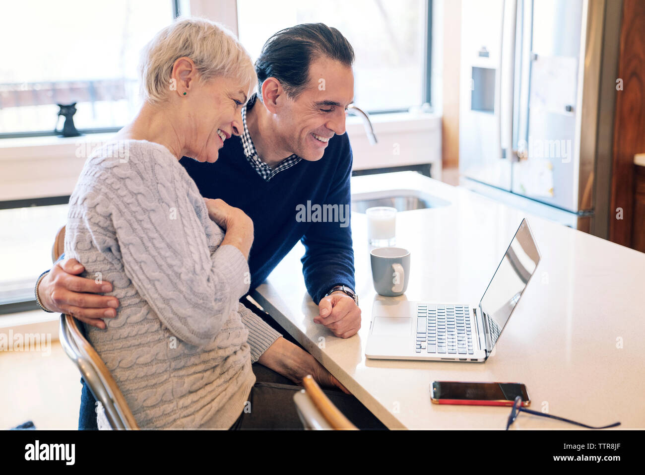 Sorridente coppia senior guardando il computer portatile mentre seduti a tavola Foto Stock