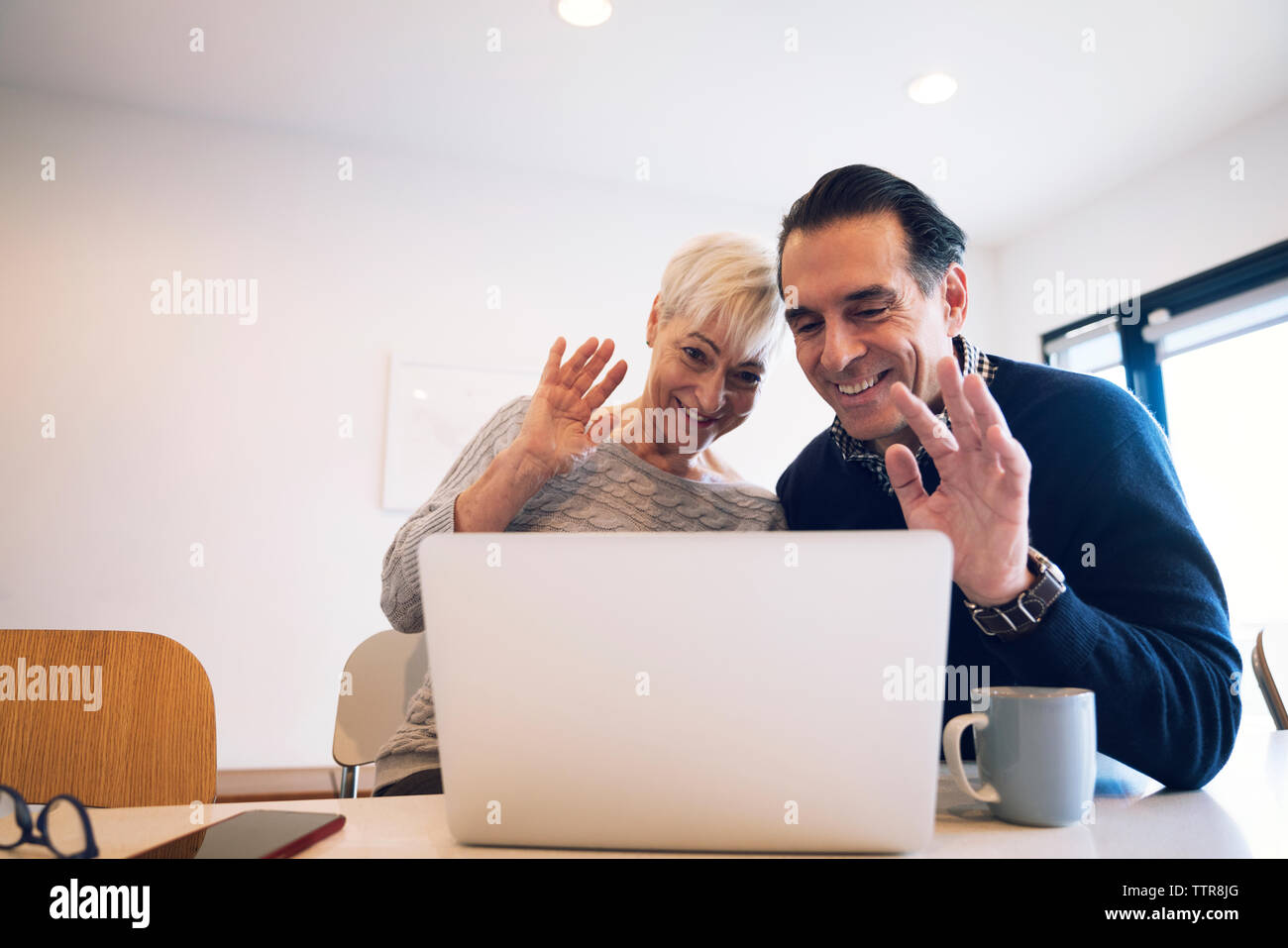 Felice coppia senior sventolare mentre guarda il computer portatile in casa Foto Stock