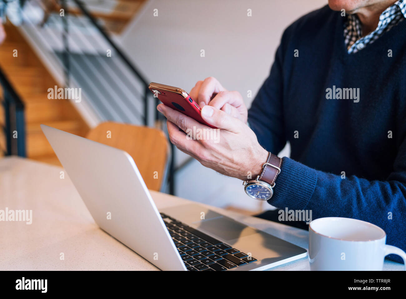 Sezione mediana dell'uomo utilizzando smart phone durante l udienza dal computer portatile al tavolo Foto Stock