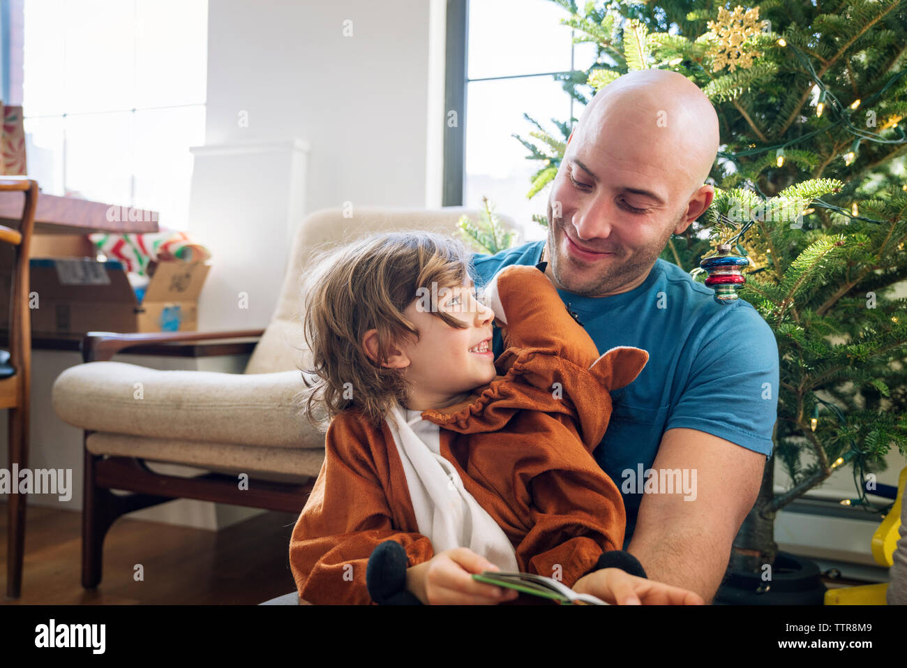 Padre felice che guarda il figlio vestito in costume contro l'albero di natale a casa Foto Stock