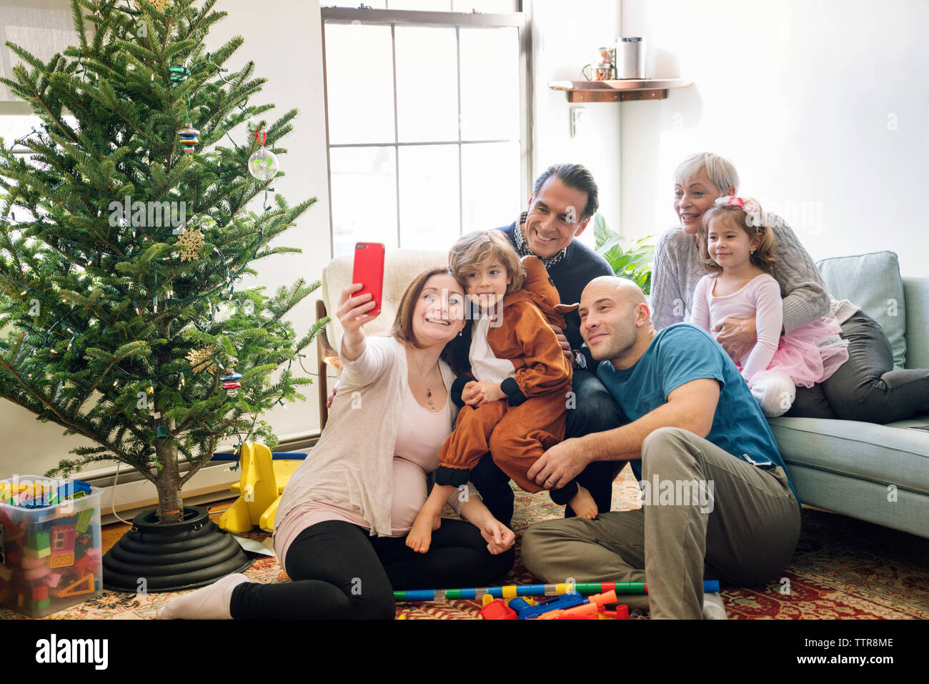 Donna incinta che fa selfie mentre è seduta con la famiglia vicino all'albero di natale a casa Foto Stock