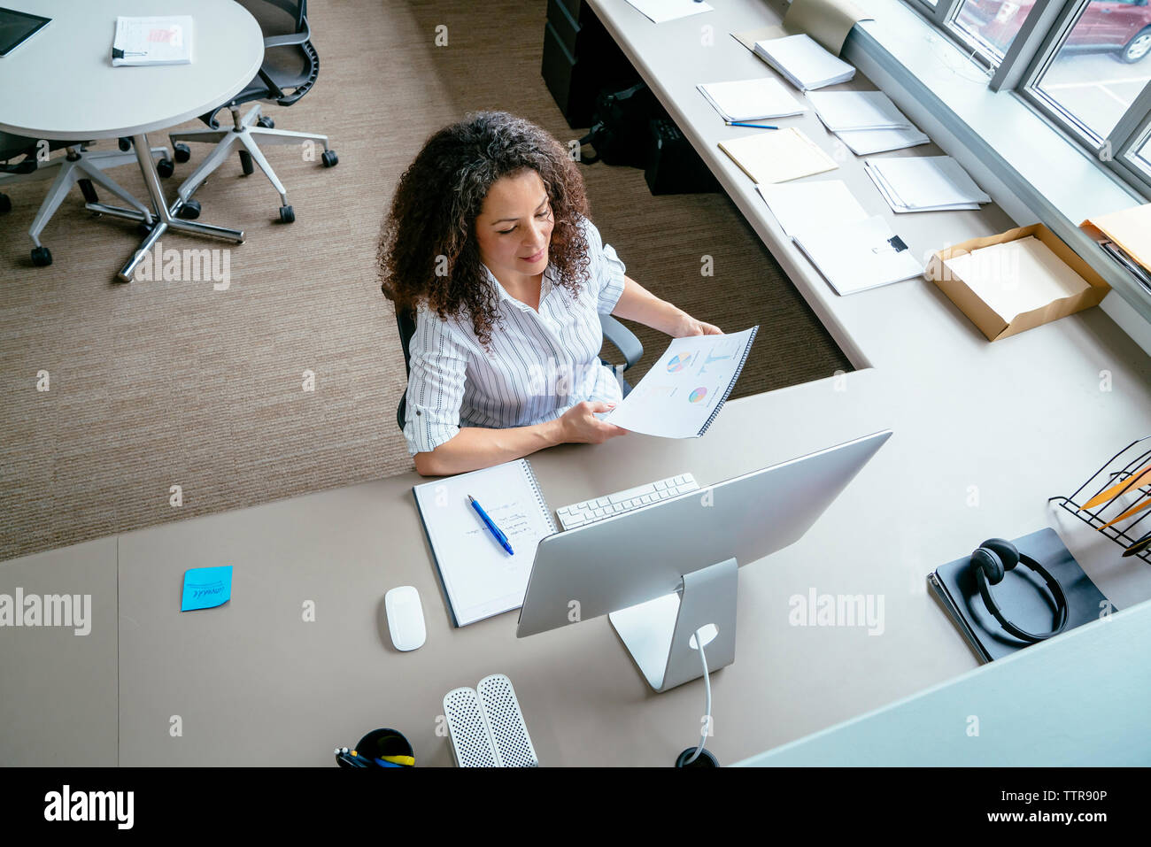 Angolo di alta vista di imprenditrice analizzando i rapporti mentre è seduto alla scrivania in ufficio Foto Stock