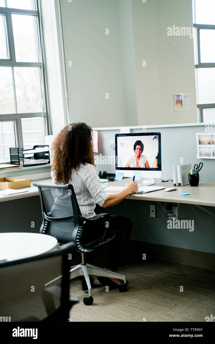 Vista posteriore di imprenditrice videoconferenza con il collega di sesso femminile su computer desktop in ufficio Foto Stock