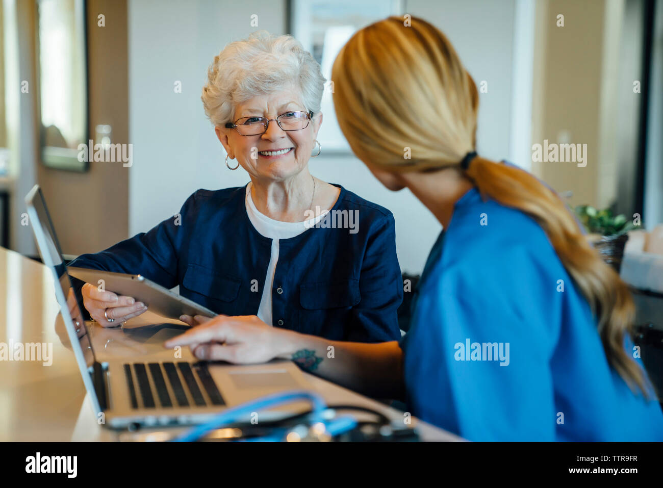 Felice senior donna che guarda a casa il caregiver tenendo computer tablet Foto Stock