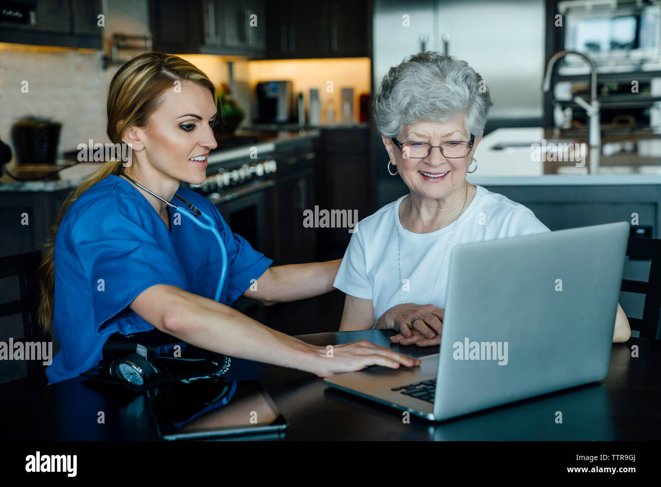 Home caregiver e senior donna guardando il computer portatile sul tavolo da pranzo Foto Stock