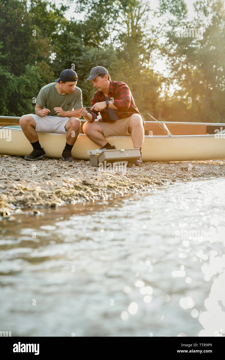 Amici di sesso maschile di regolazione delle aste di pesca stando seduti in barca sul lago di garda Foto Stock