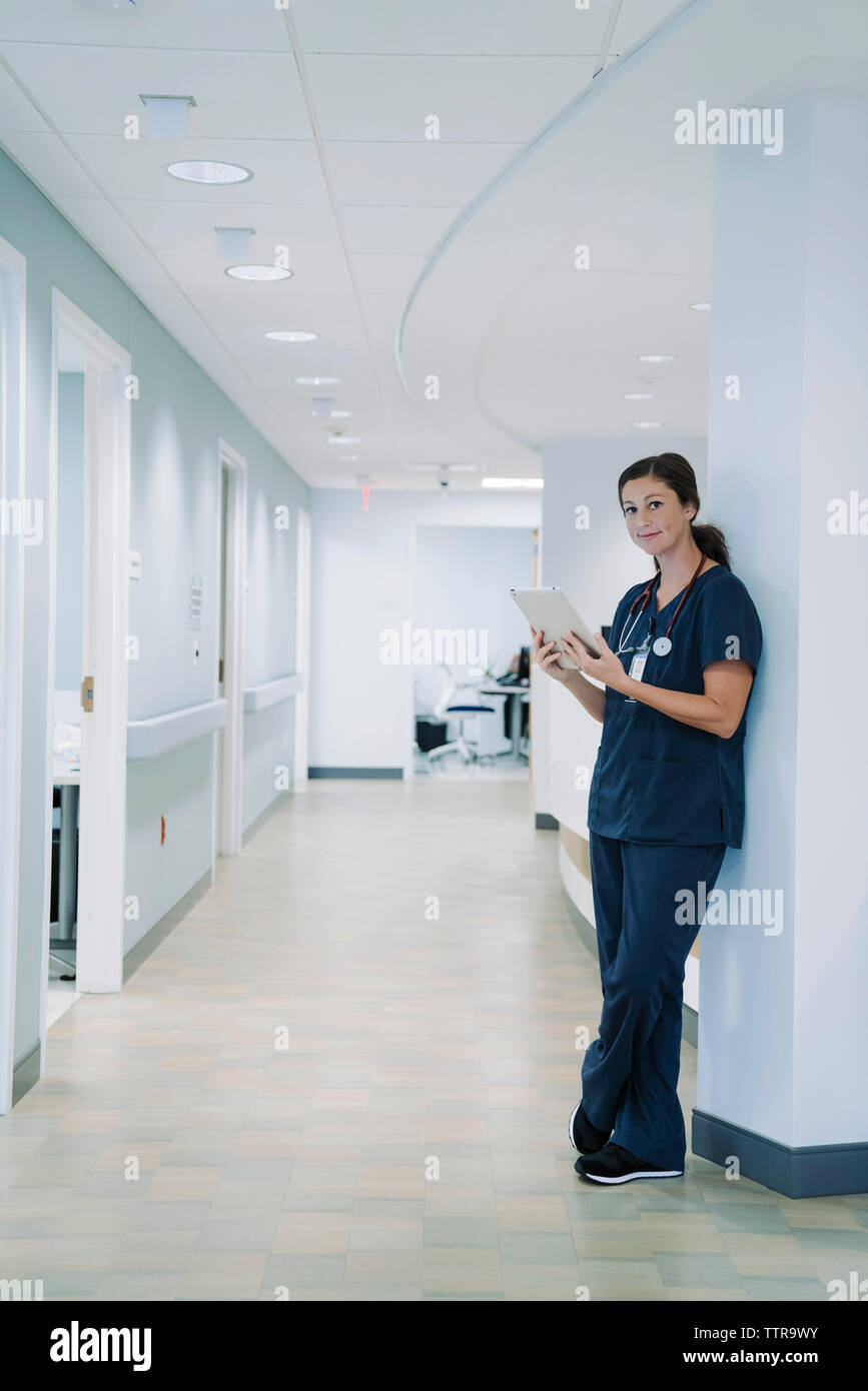 Ritratto di medico donna utilizzando computer tavoletta mentre appoggiata contro la colonna architettonica in ospedale Foto Stock