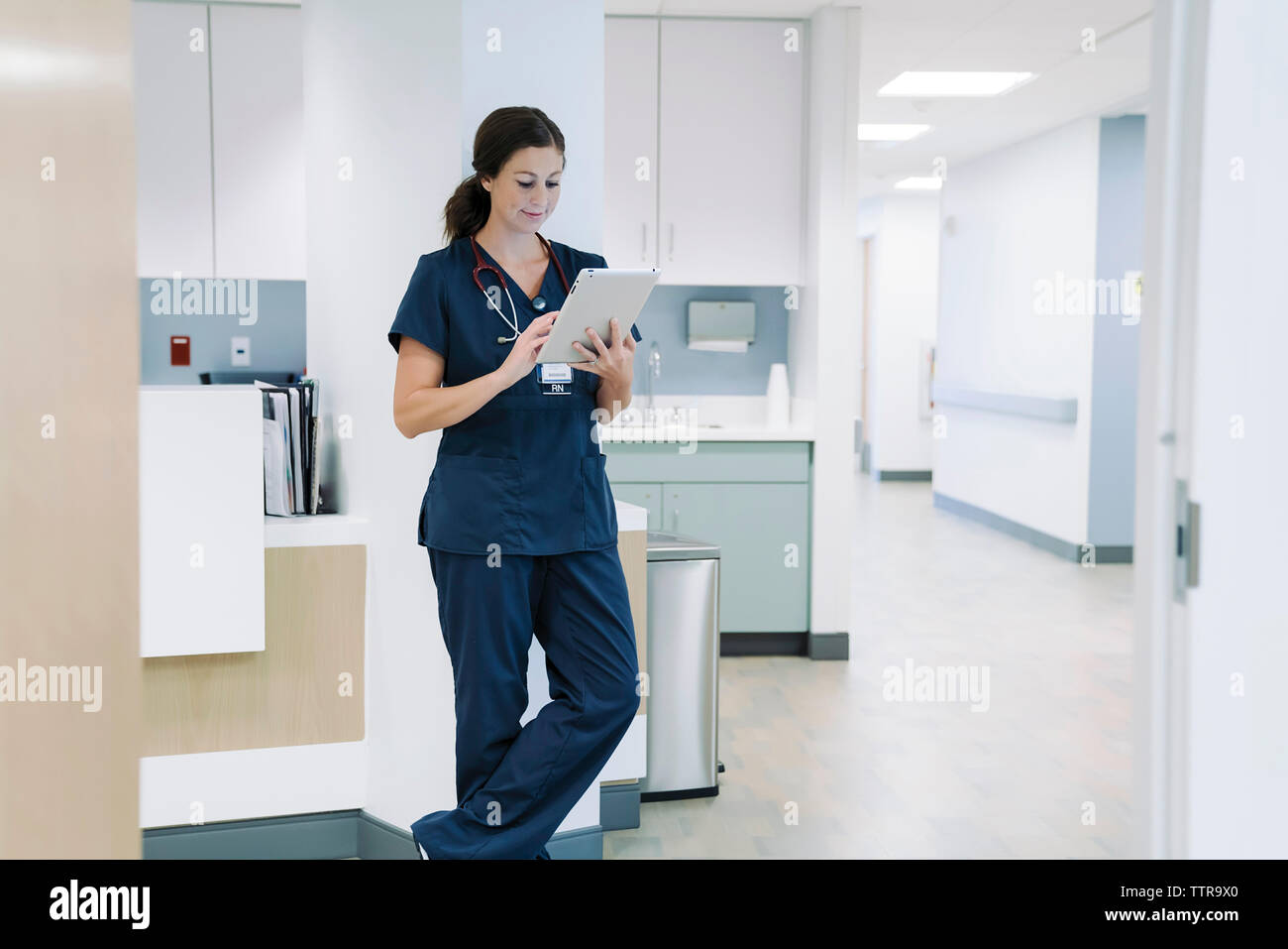 Medico donna utilizzando computer tavoletta mentre appoggiata contro la colonna architettonica in ospedale Foto Stock