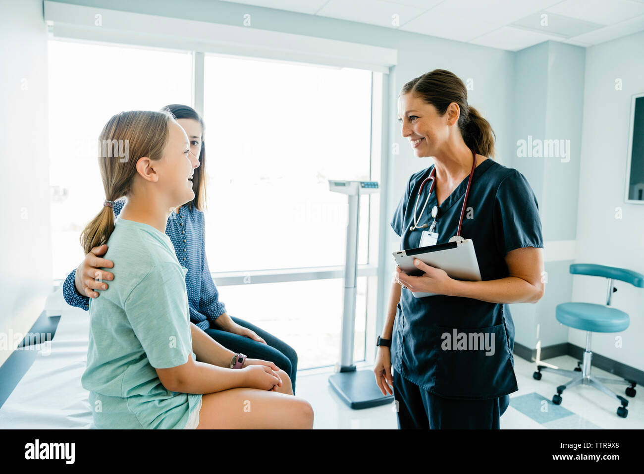 Allegro ragazza guardando il pediatra seduti dalla madre sul lettino in ospedale Foto Stock