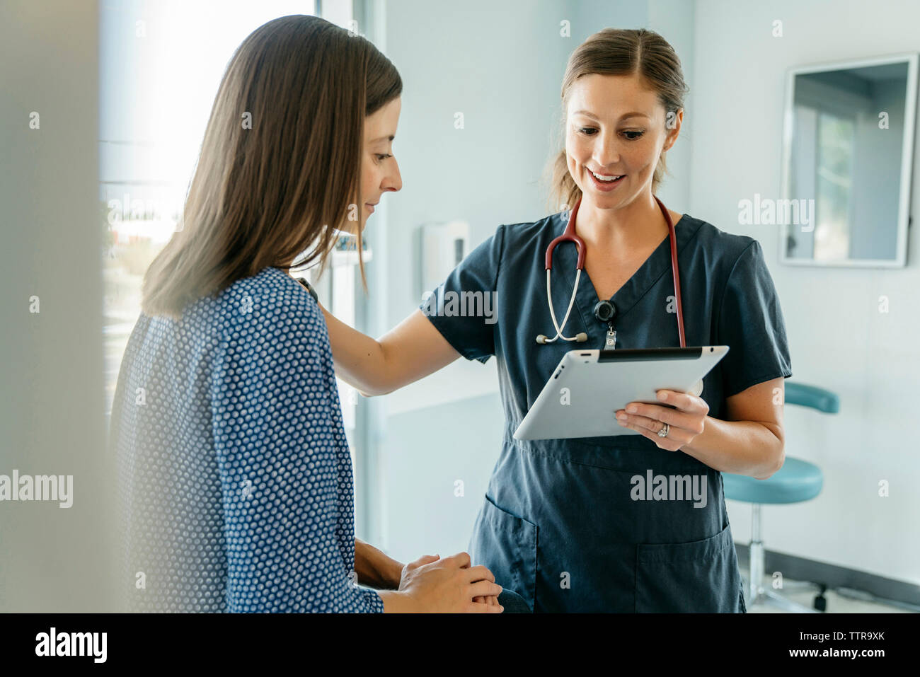 Medico donna consolante mentre mostra computer tablet in medical sala esame Foto Stock