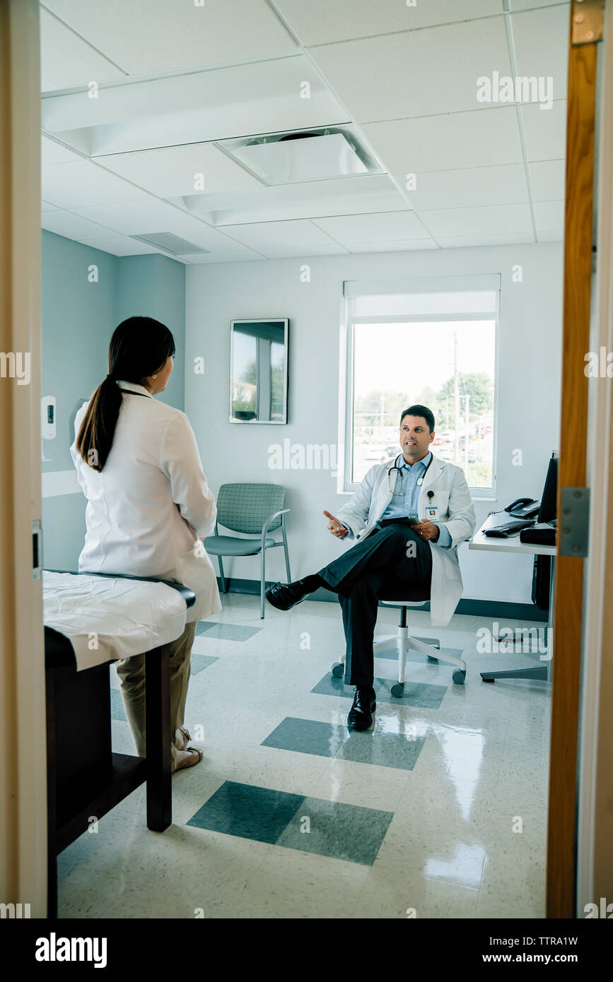 Medico per discutere con il collega di sesso femminile mentre si lavora nella sala esame visto attraverso la porta Foto Stock