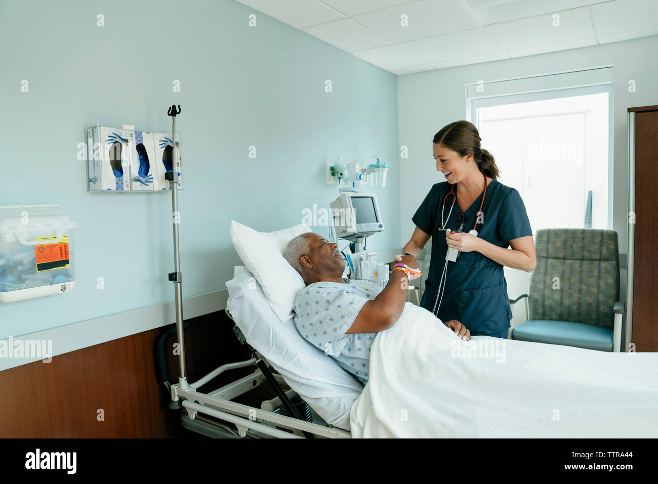 Handshaking infermiere con senior paziente sdraiato sul letto in ospedale Foto Stock
