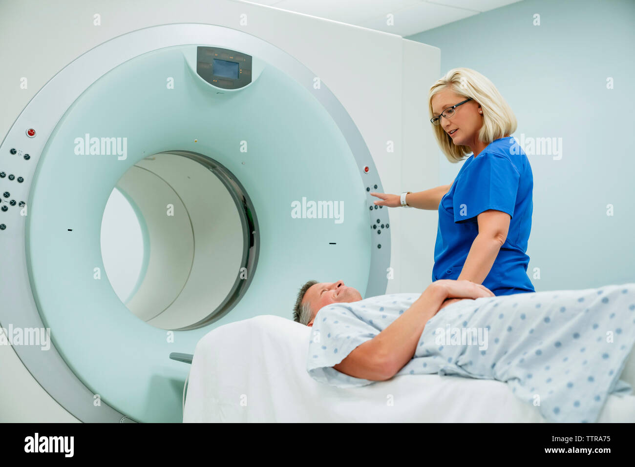 L'infermiera guardando il paziente sdraiato su scanner MRI mentre preme il pulsante start nella sala esame Foto Stock