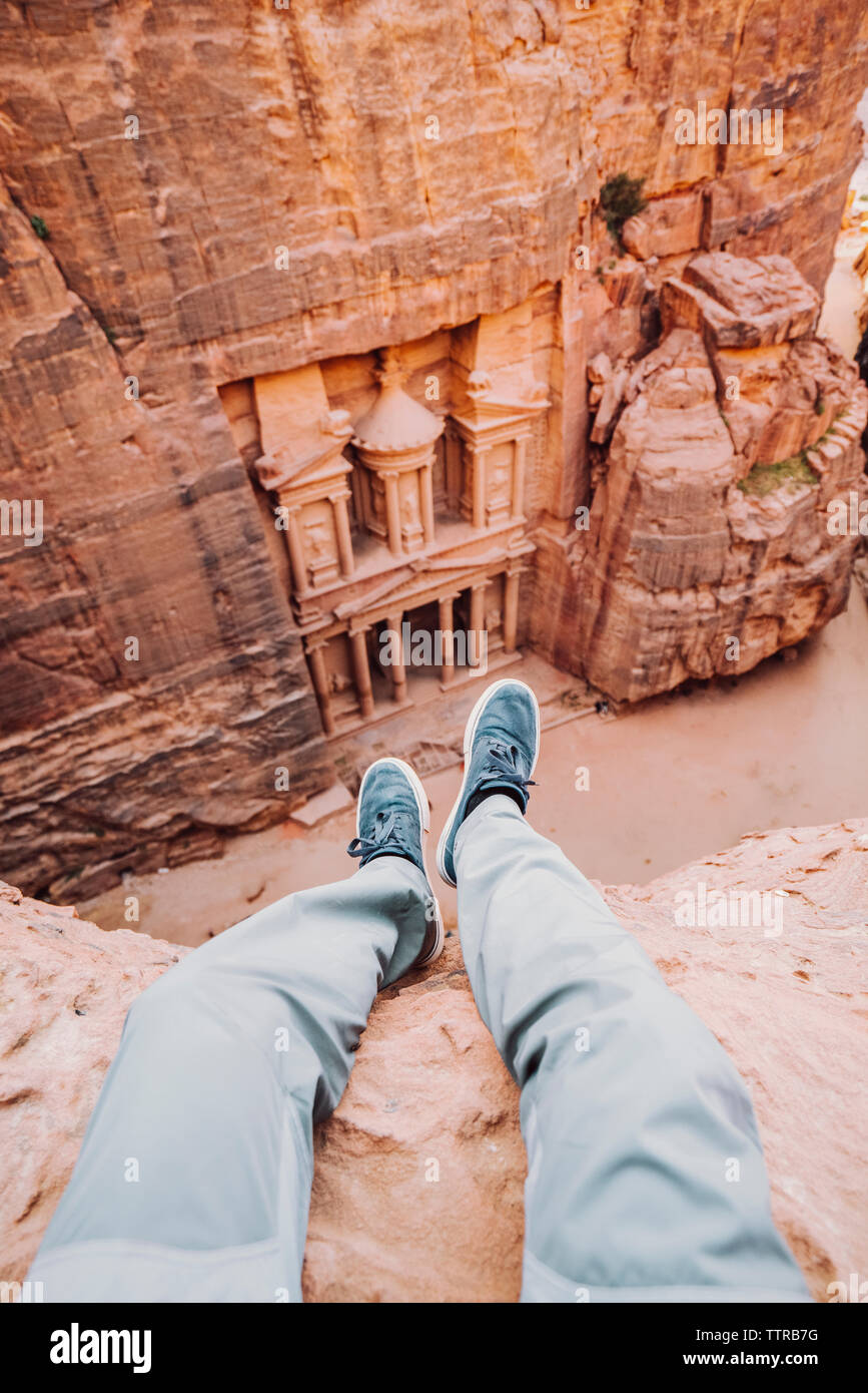 Sezione bassa di uomo seduto sulla scogliera contro Al-Khazneh di Petra Foto Stock