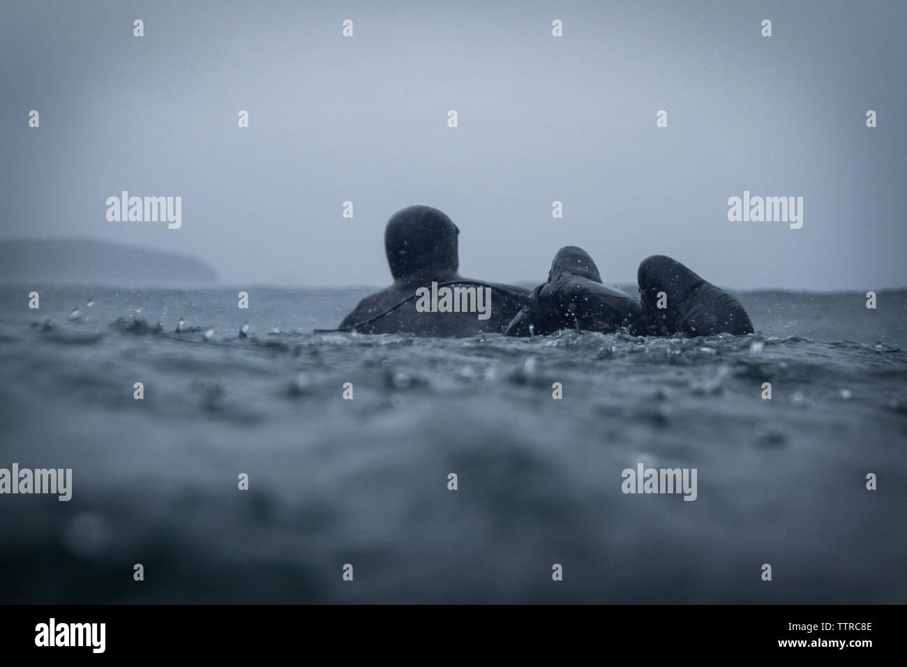 Vista posteriore dell'uomo surf in mare contro il cielo durante la stagione delle piogge Foto Stock