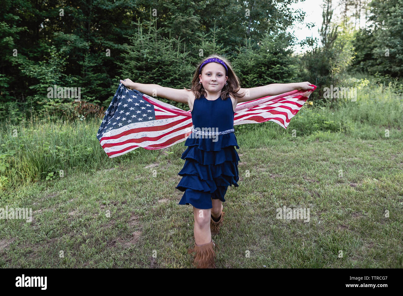 Ritratto di sorridente ragazza con bandiera americana mentre si cammina sul campo erboso Foto Stock