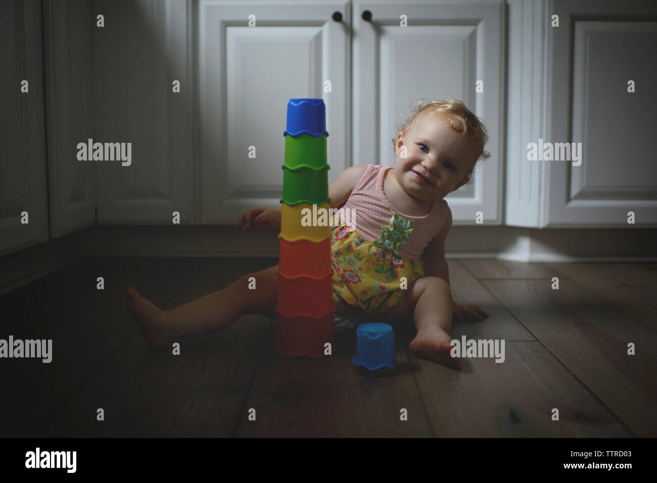 Ritratto di simpatici baby girl con giocattoli colorati mentre è seduto sul pavimento di legno a casa Foto Stock