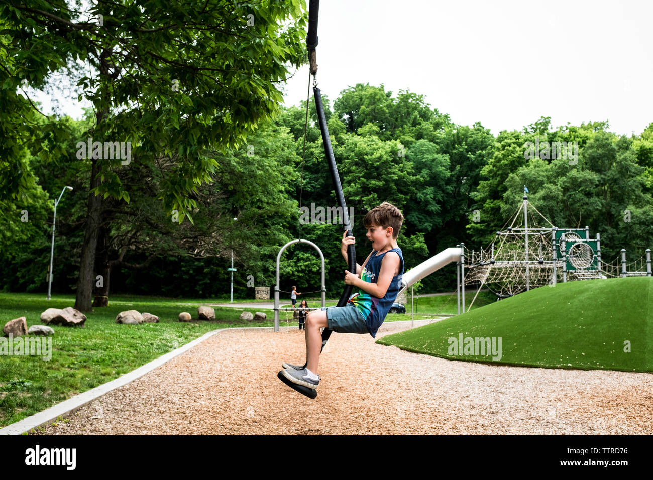 Vista laterale del ragazzo spensierate giocando su swing sul parco giochi Foto Stock